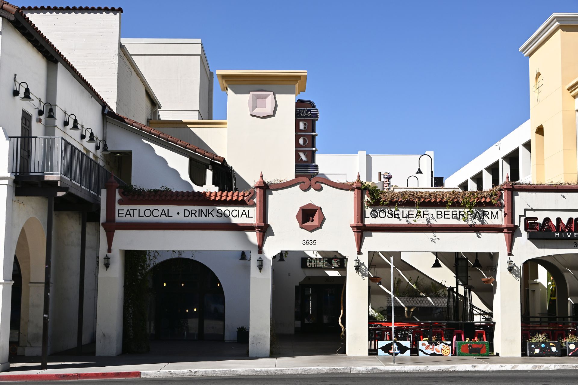 Spanish-style building with archways and storefronts under a blue sky.