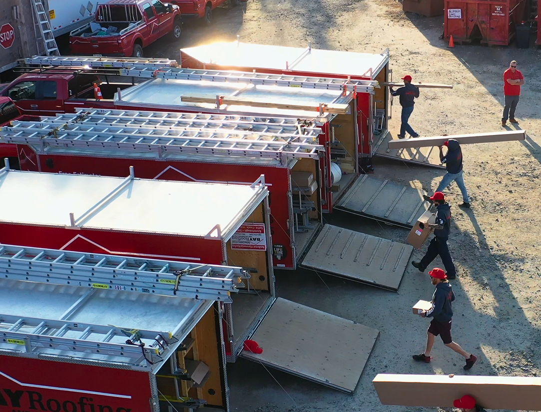 Red pickup truck towing a red trailer on a dirt road through a forest.