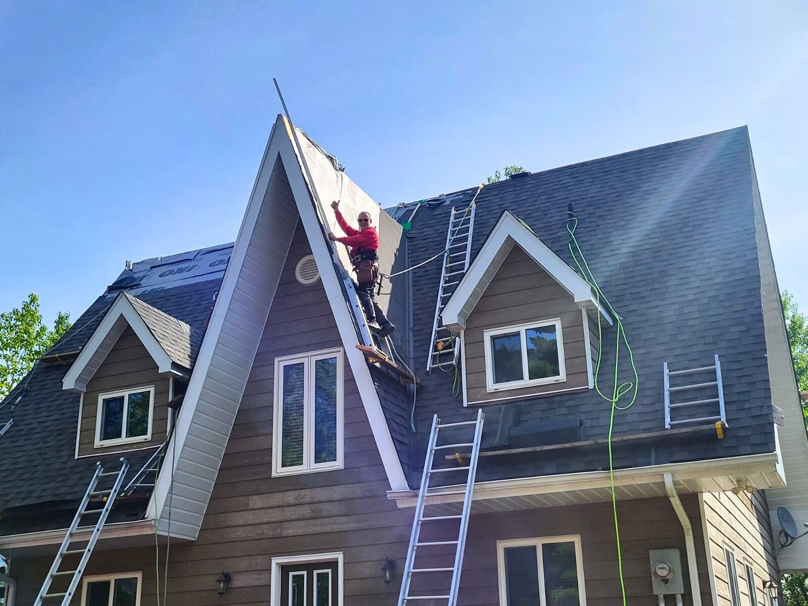 Two workers on ladders repairing a steep roof on a house under a blue sky