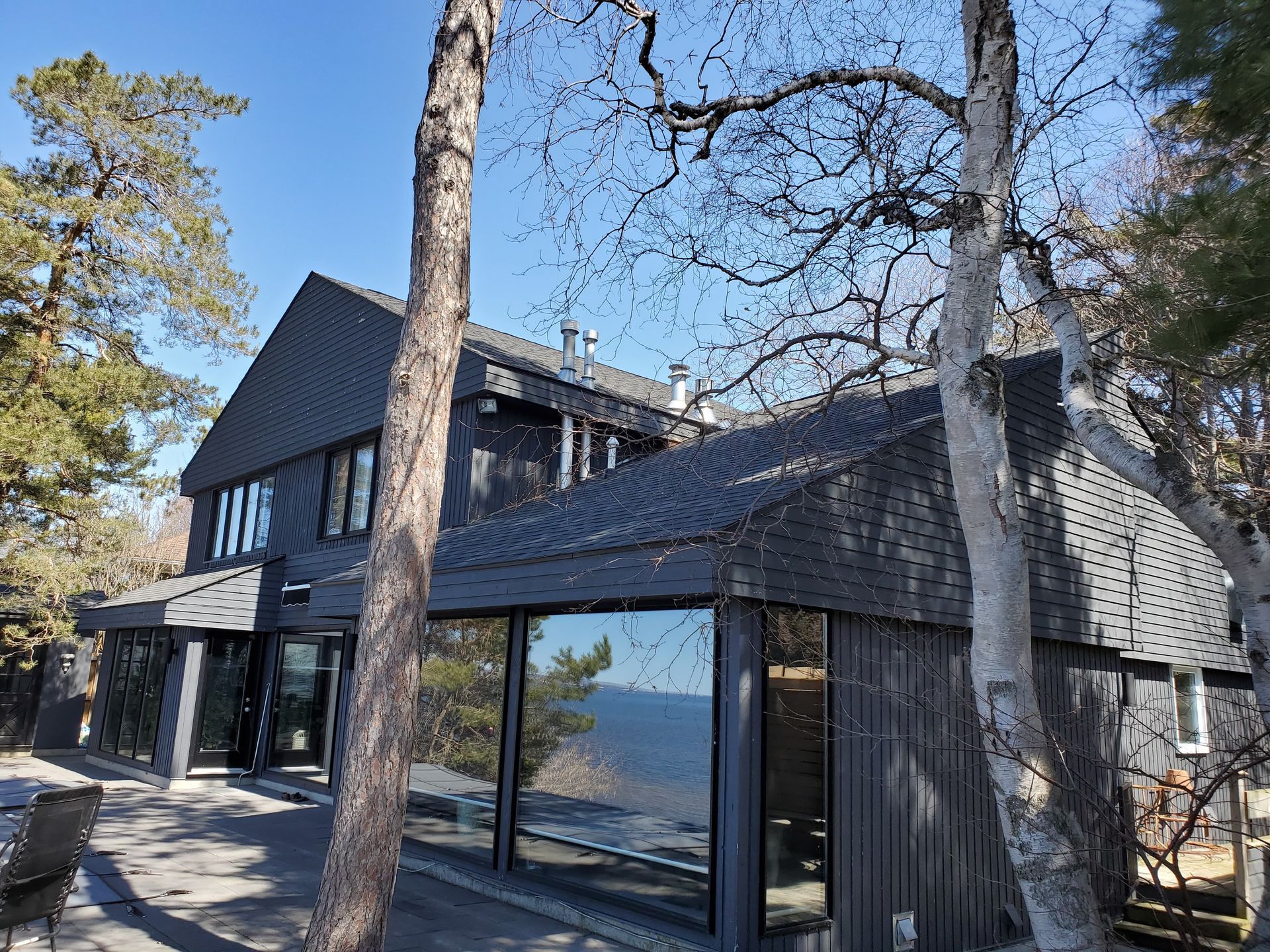 Dark gray house with large windows, trees, and a view of water.