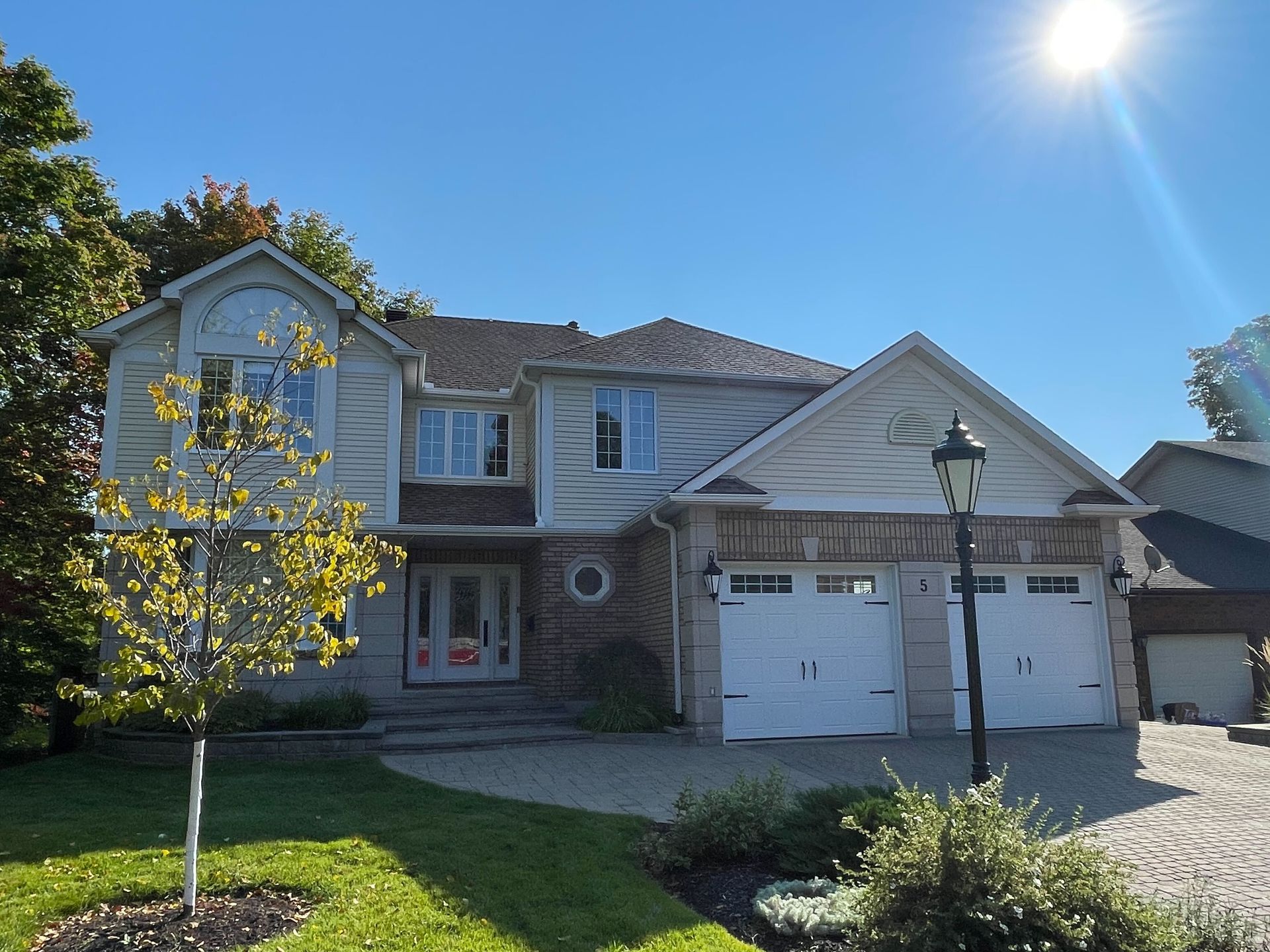 Two-story house with a two-car garage, front yard, and bright sun in a clear sky.