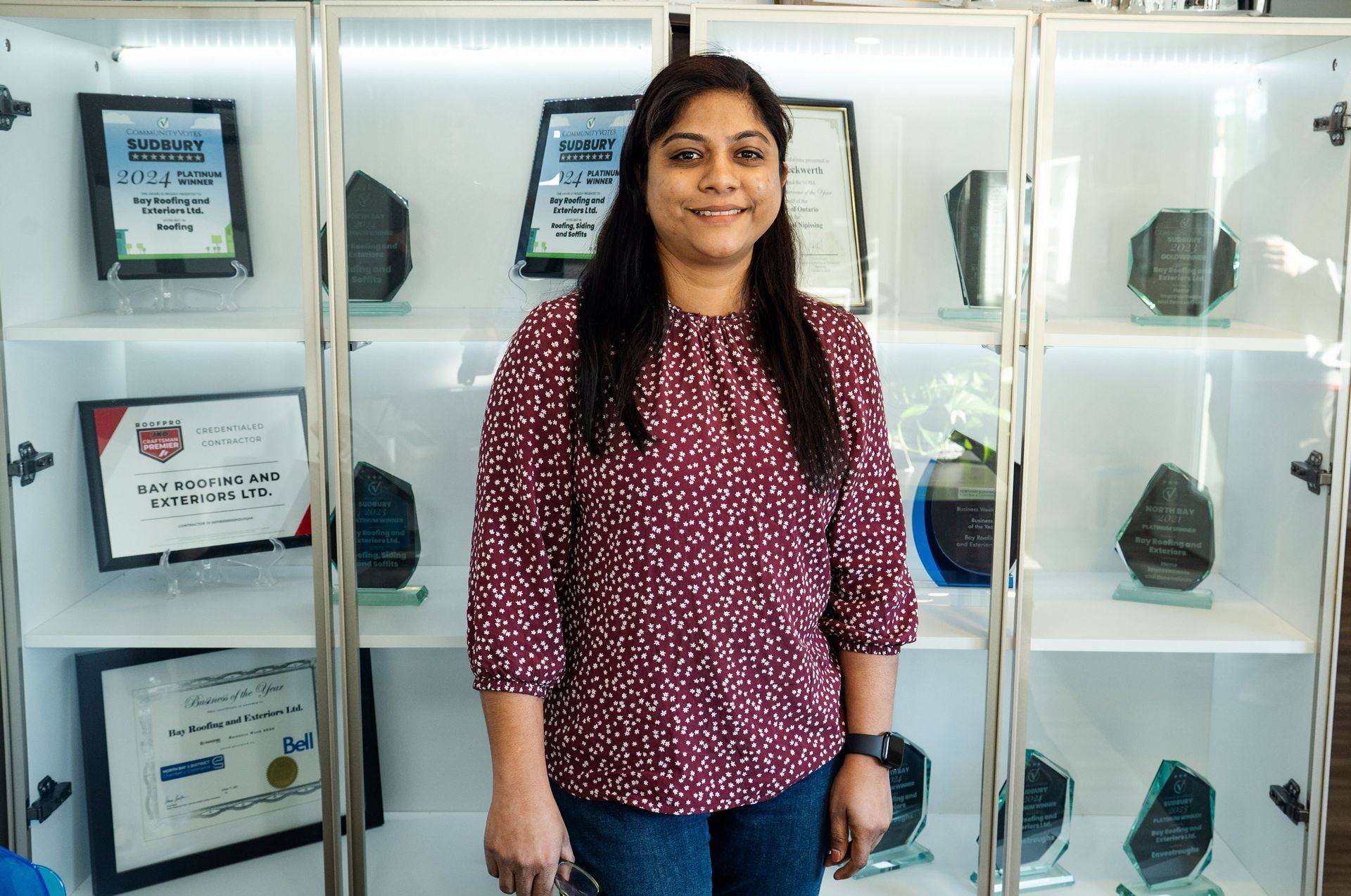 Woman in burgundy shirt, smiling, standing in front of display case with awards.