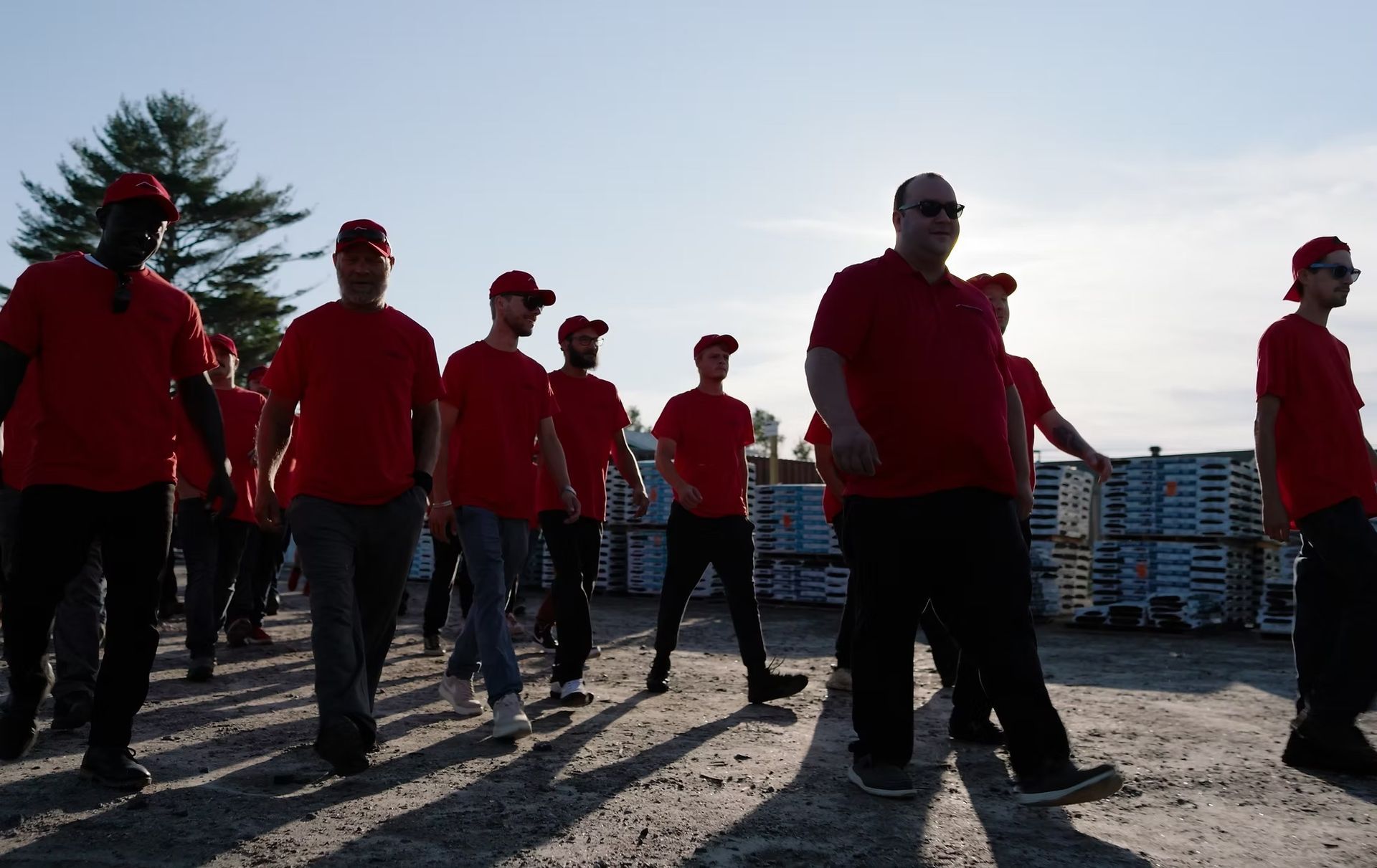 Group of people in red shirts and hats walking on a gravel surface outdoors.