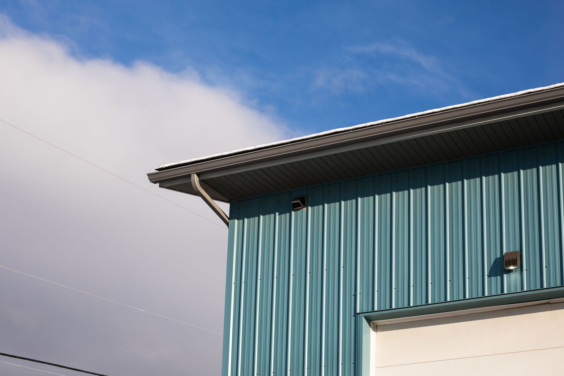Blue metal building with gray roof and gutter against a blue sky with clouds.