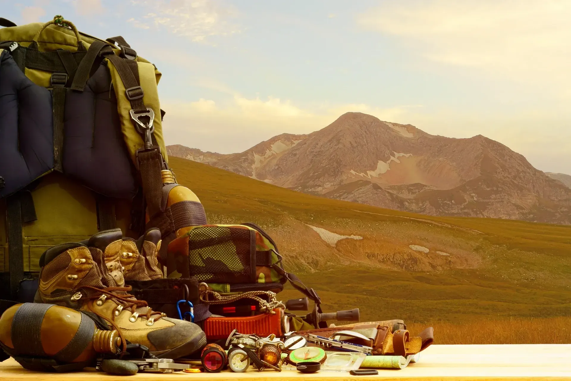 A backpack and hiking boots are on a table with mountains in the background