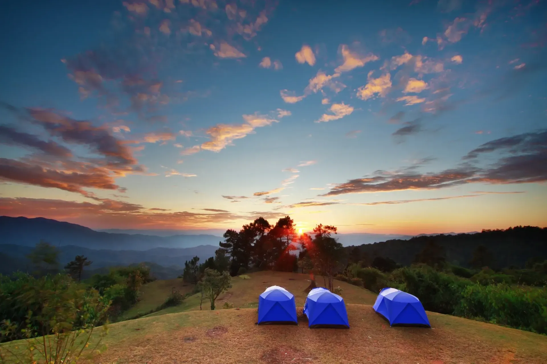 Three tents are sitting on top of a hill at sunset.