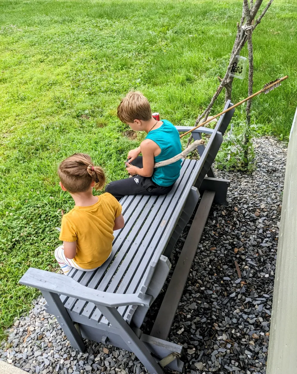 Two children are sitting on a swing in the grass.