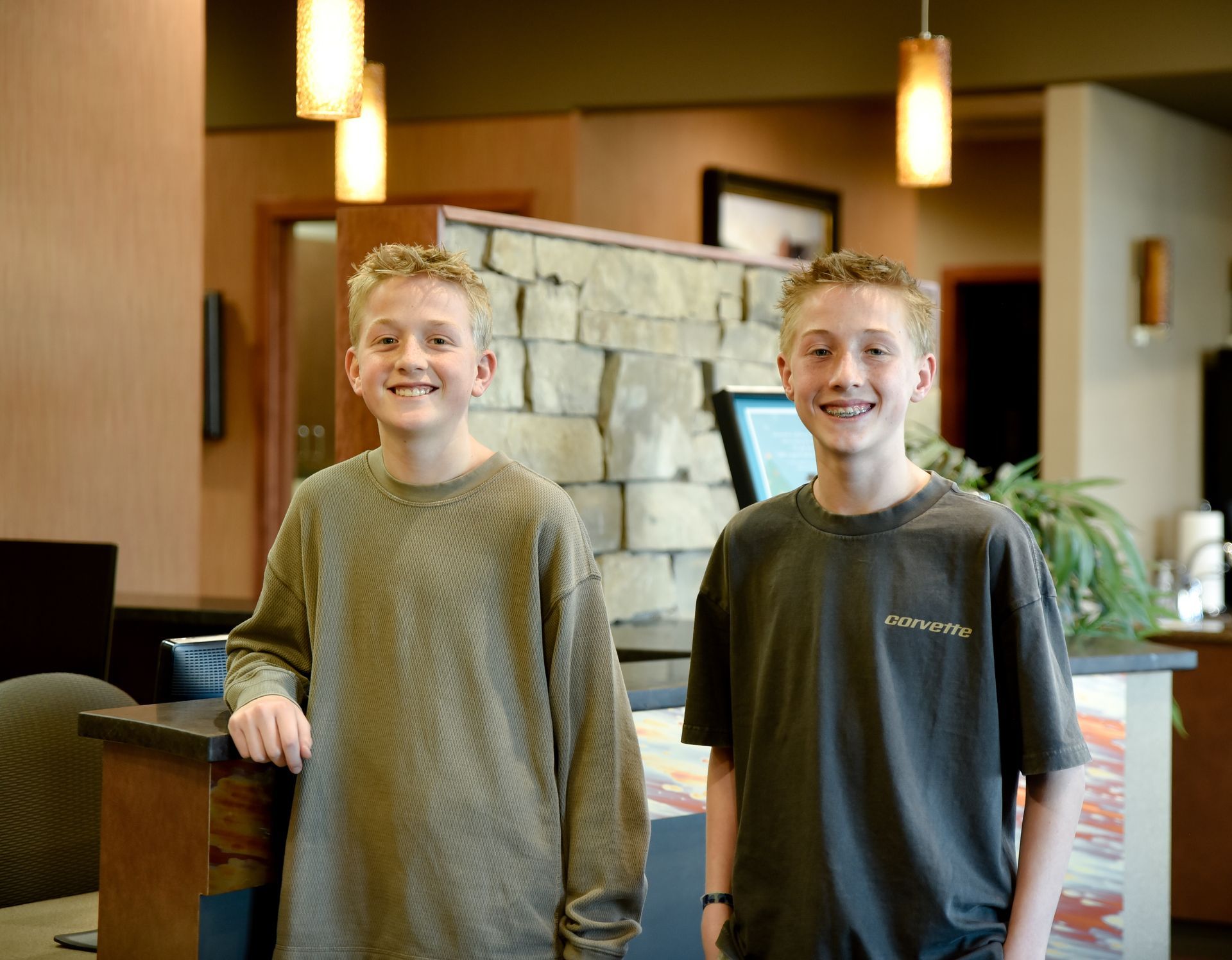 Two smiling individuals stand side by side in a well-lit indoor lobby with a stone wall backdrop.