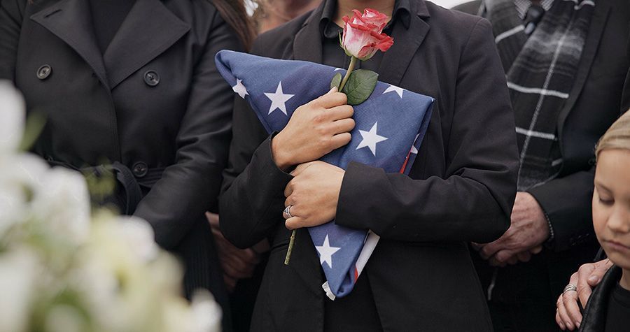 Woman holding folded American flag at funeral with single rose
