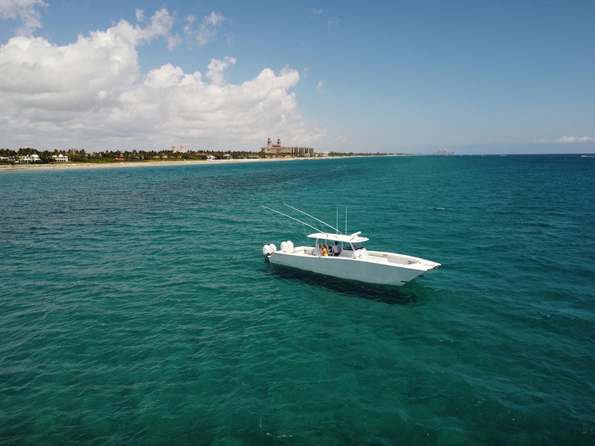 White motorboat on turquoise water near a sandy shoreline under a partly cloudy sky