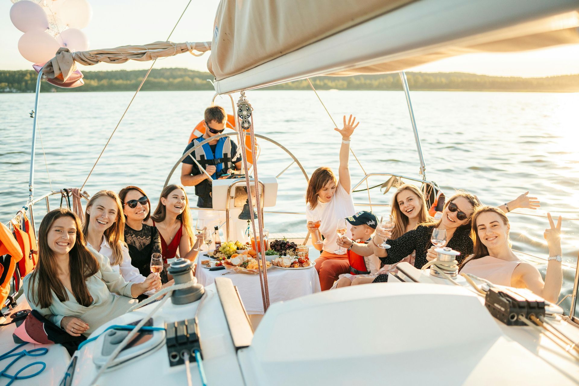 People lounging on a sailboat at sunset with drinks and balloons on calm water