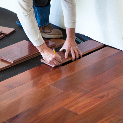 A man is measuring a piece of wood on a hardwood floor.