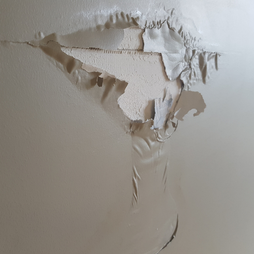 A close up of a wall with peeling paint and a hole in it.