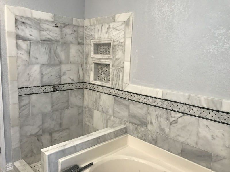 A bathroom with a tub and a shower with marble tiles.
