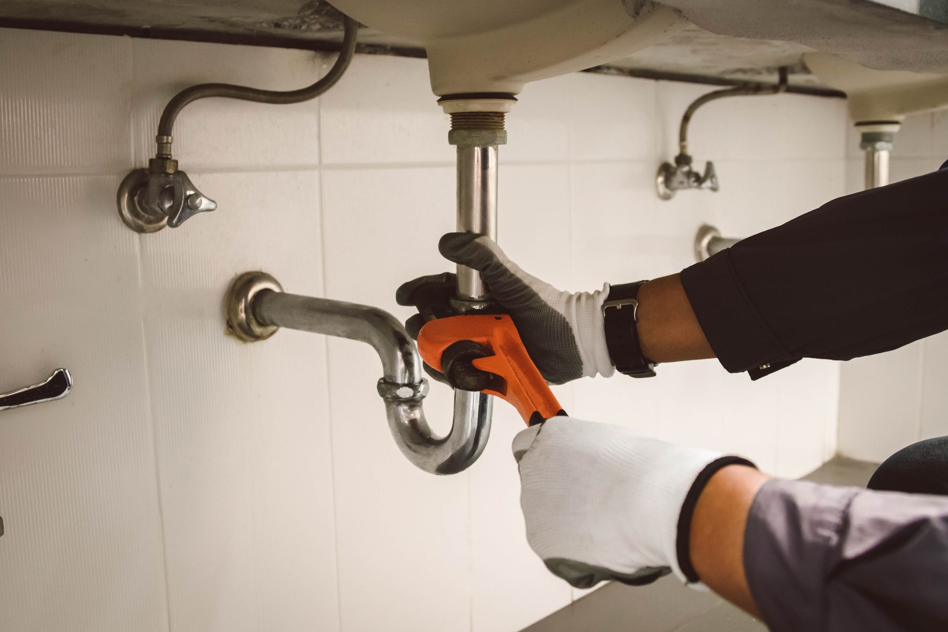 Close-up of hands tightening the sink pipe with an orange wrench.