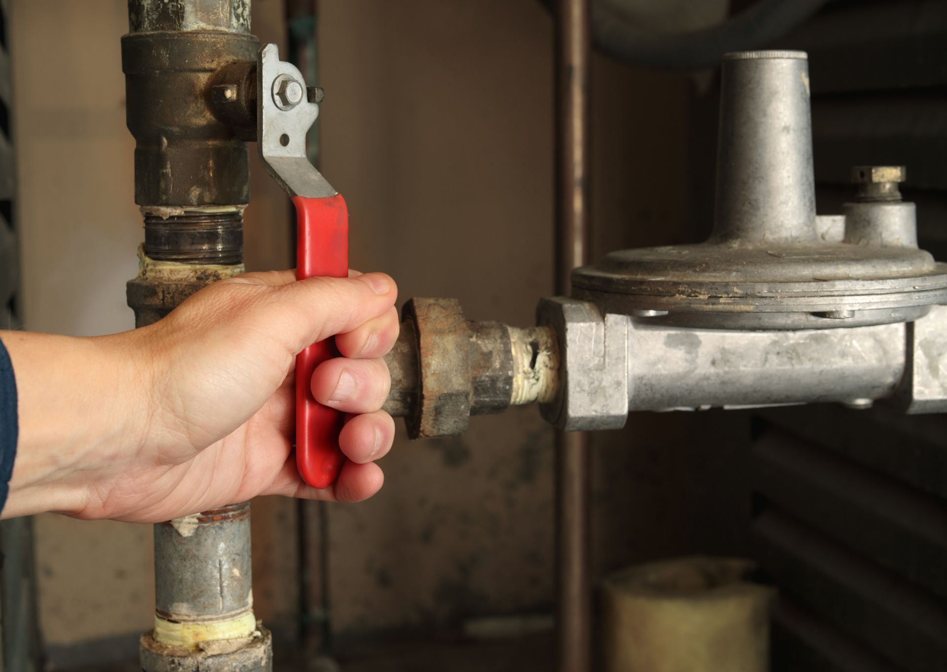 A hand holds and uses a red shut-off valve on the pipes of a pressure gas regulator.