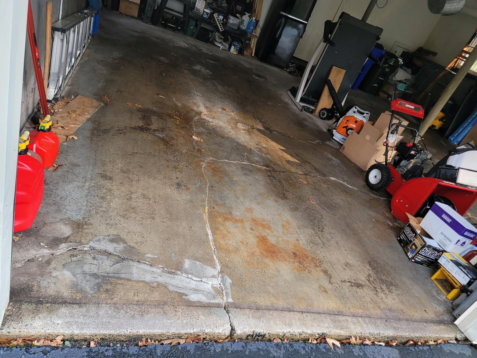 Concrete garage interior with various items, including a snowblower and boxes, scattered on the floor.