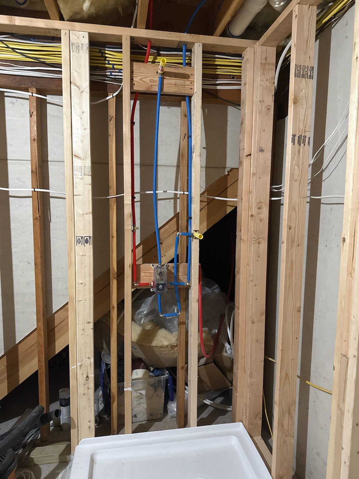 Framed wall with plumbing pipes (red, blue) and electrical wiring. A shower base is in the foreground.