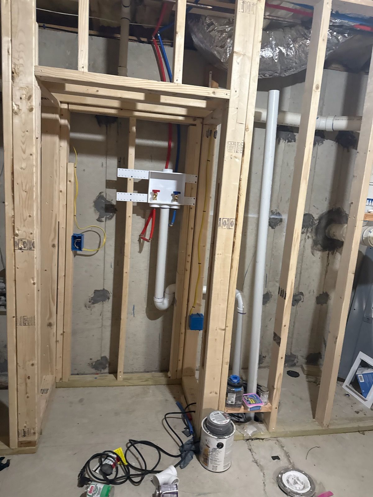 Framed-out walls with plumbing and electrical work in progress; white pipes, blue electrical boxes, and wood framing.