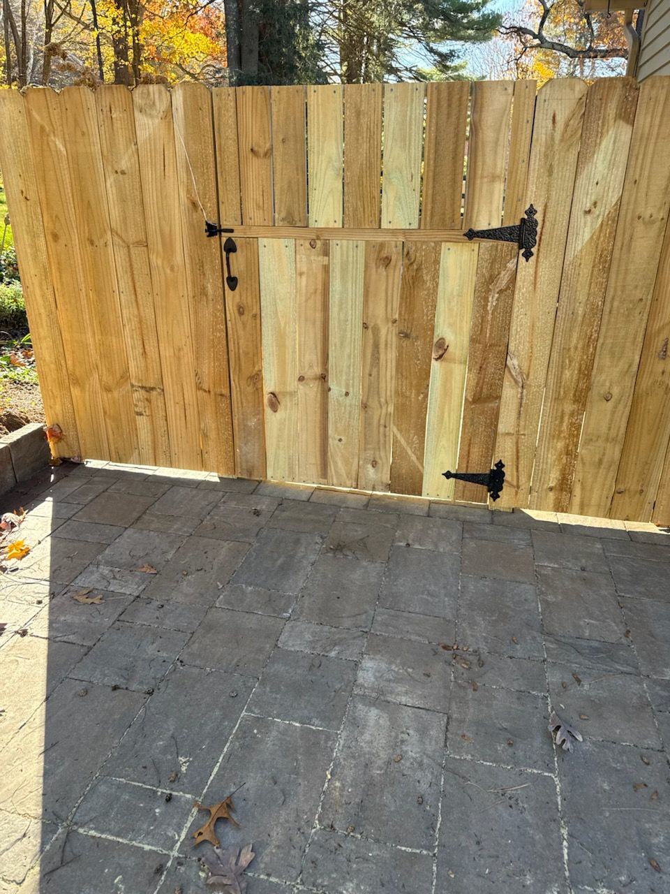 Wooden fence with a gate, black hinges and latch. Sunny outdoor setting on a brick patio.