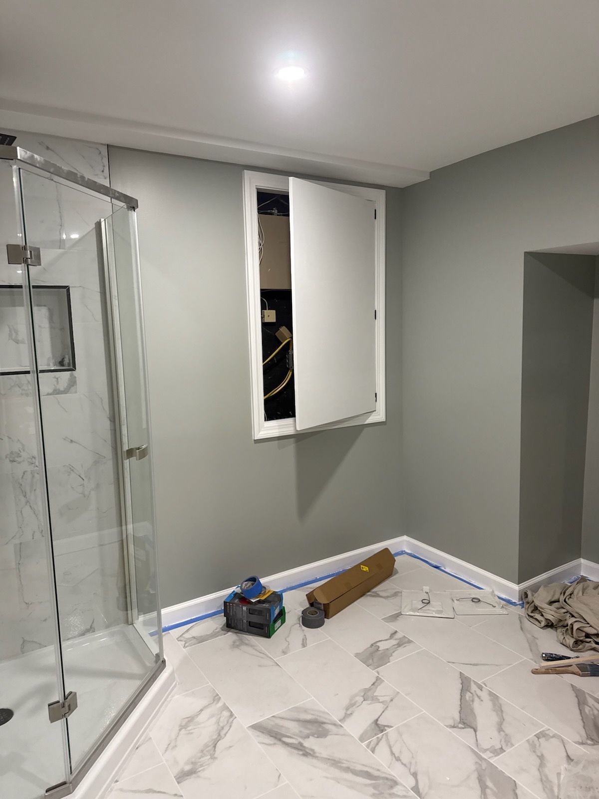 Bathroom interior with gray walls, marble tile floor, shower stall, and electrical panel behind a hinged door.