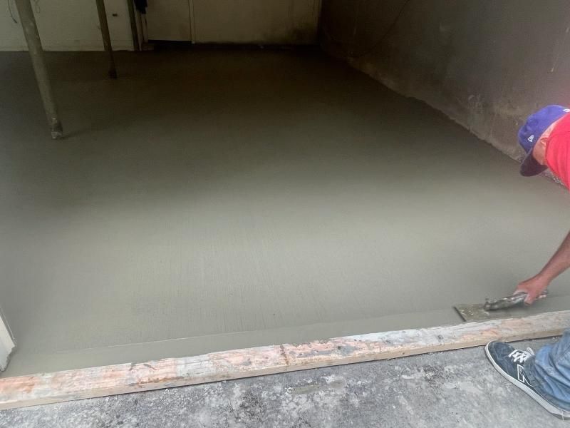 Man smoothing fresh concrete floor with a trowel in a room.