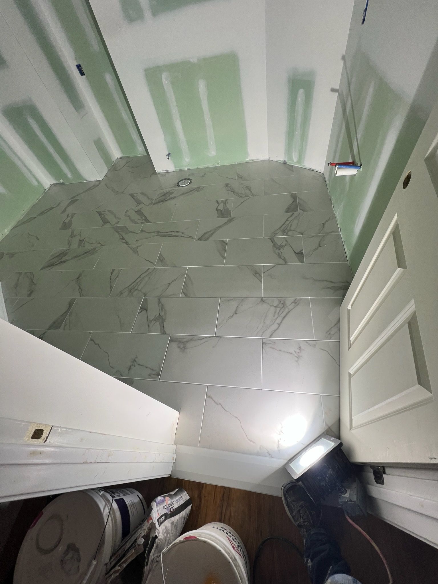Bathroom renovation in progress, featuring tile floor, green sheetrock, buckets, and a work light.