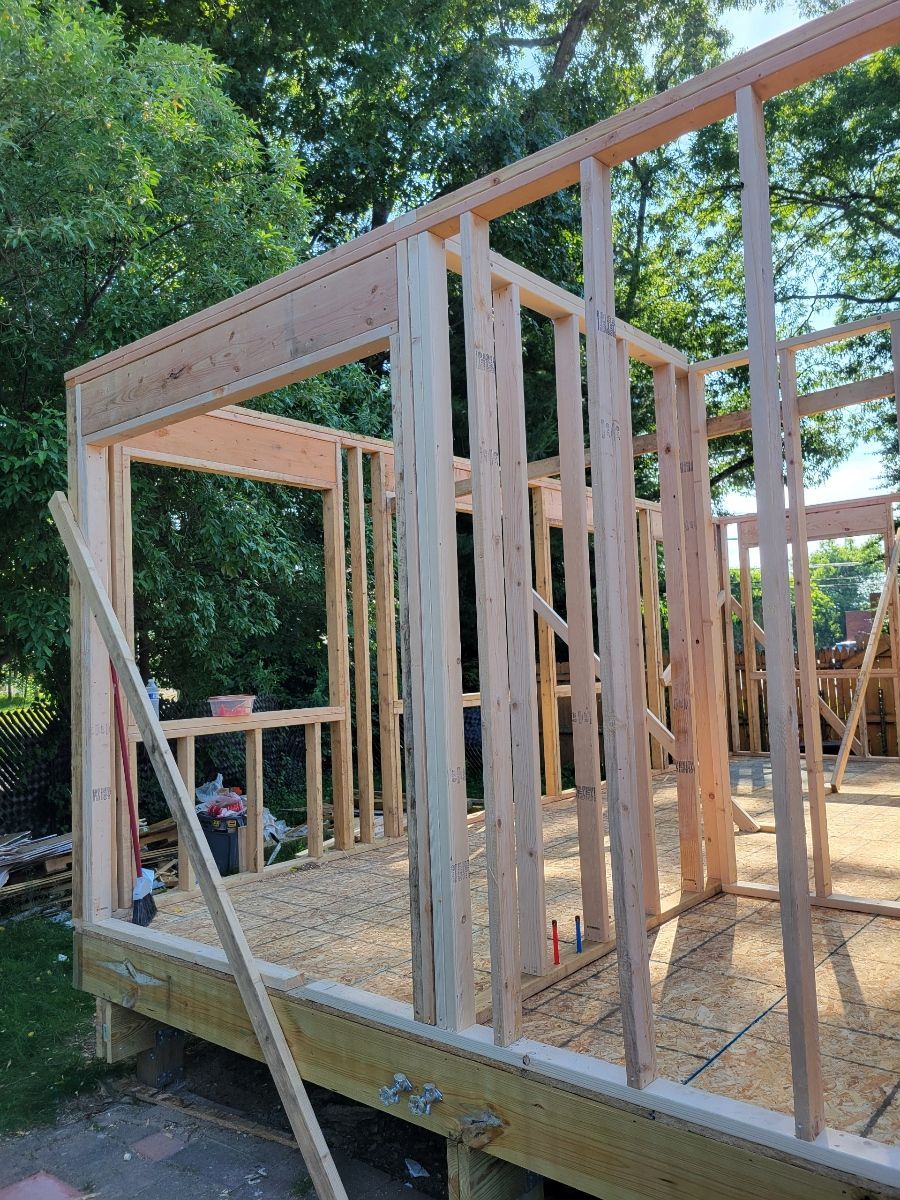 A wooden structure is being built in a yard with trees in the background.