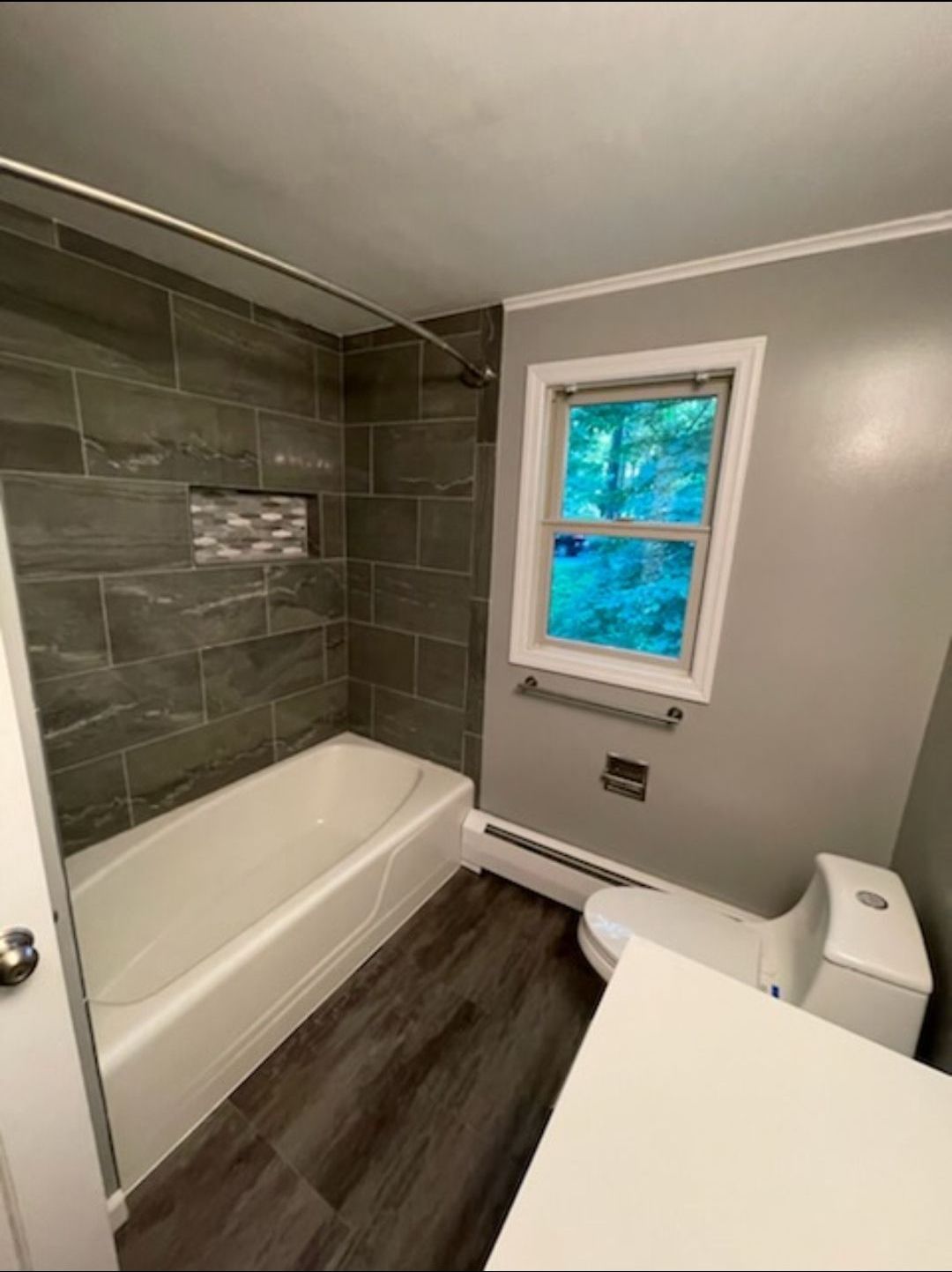 A bathroom with a tub , toilet , and window.
