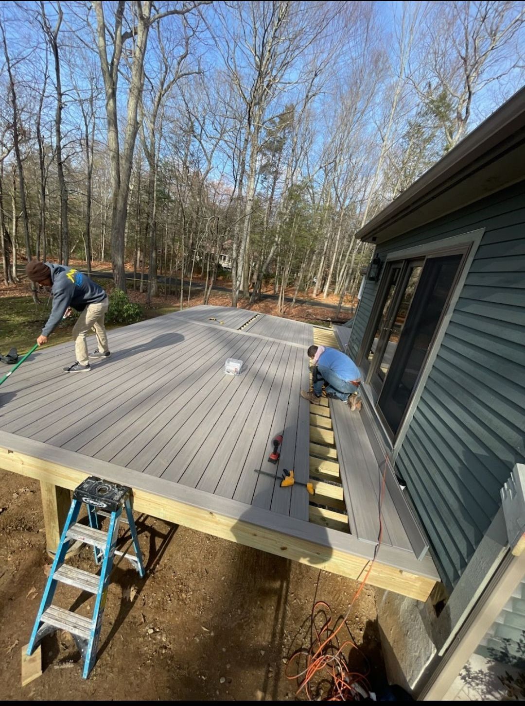 Two men are working on a wooden deck in front of a house.