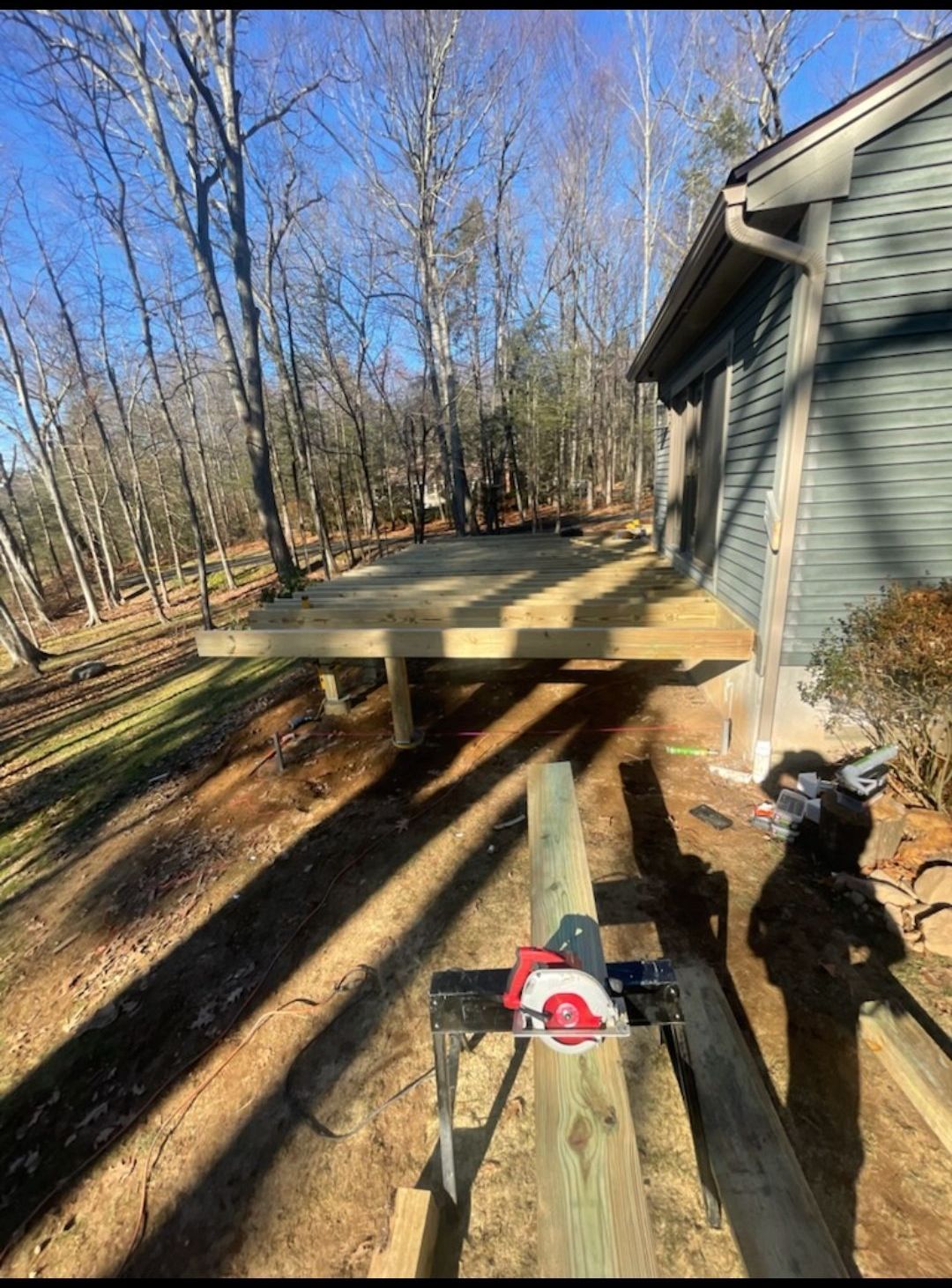 A wooden deck is being built in front of a house in the woods.