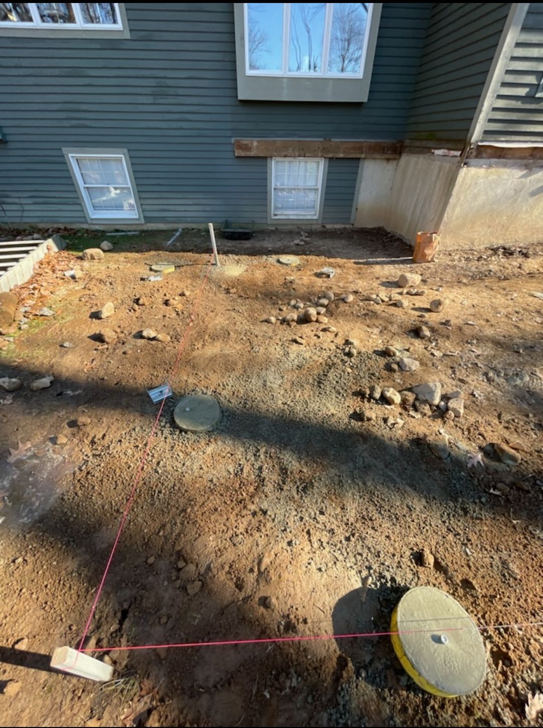 A person is using a laser to measure a hole in the ground in front of a house.