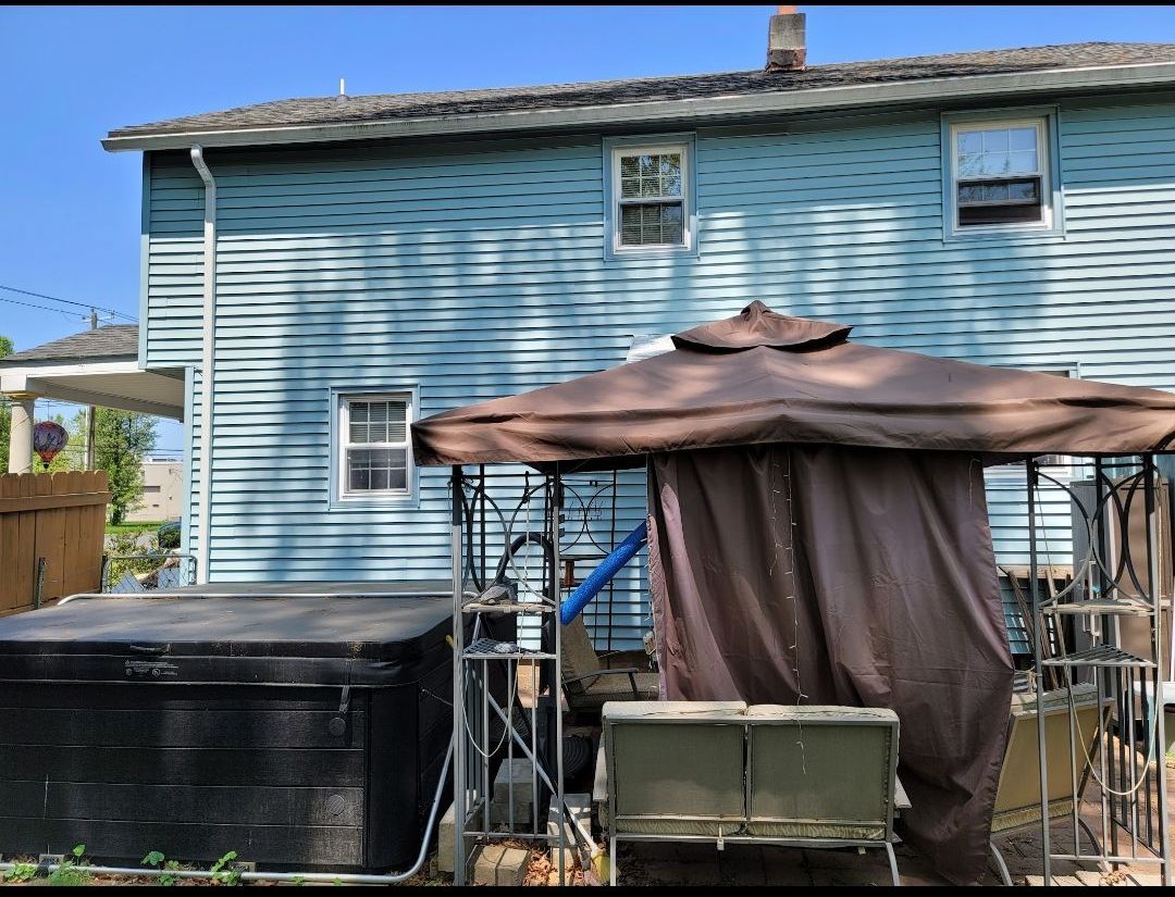 A blue house with a gazebo and a hot tub in the backyard.
