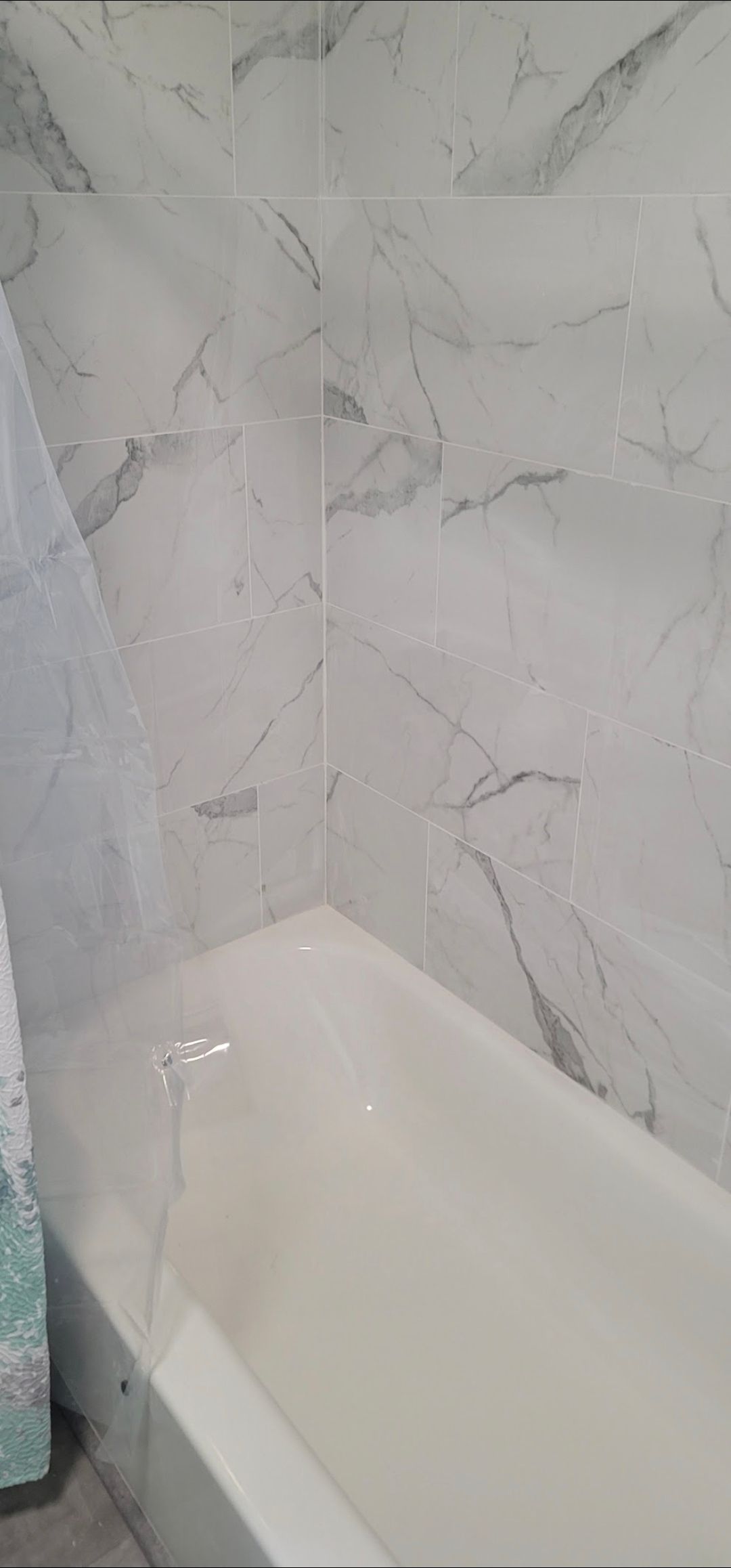 There is a bathtub in the bathroom with marble tiles on the wall.