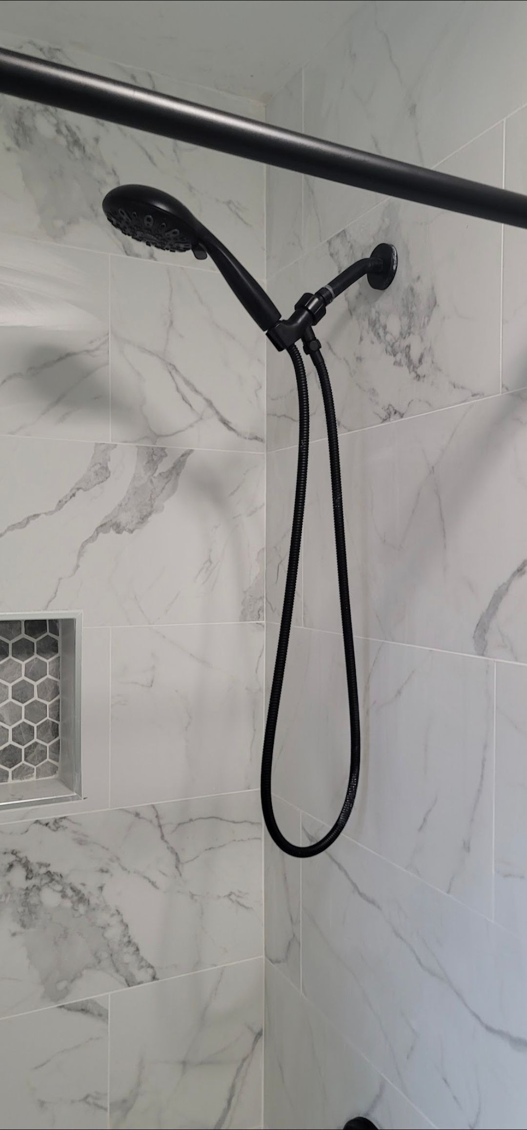 A black shower head is hanging from a black shower curtain in a bathroom.