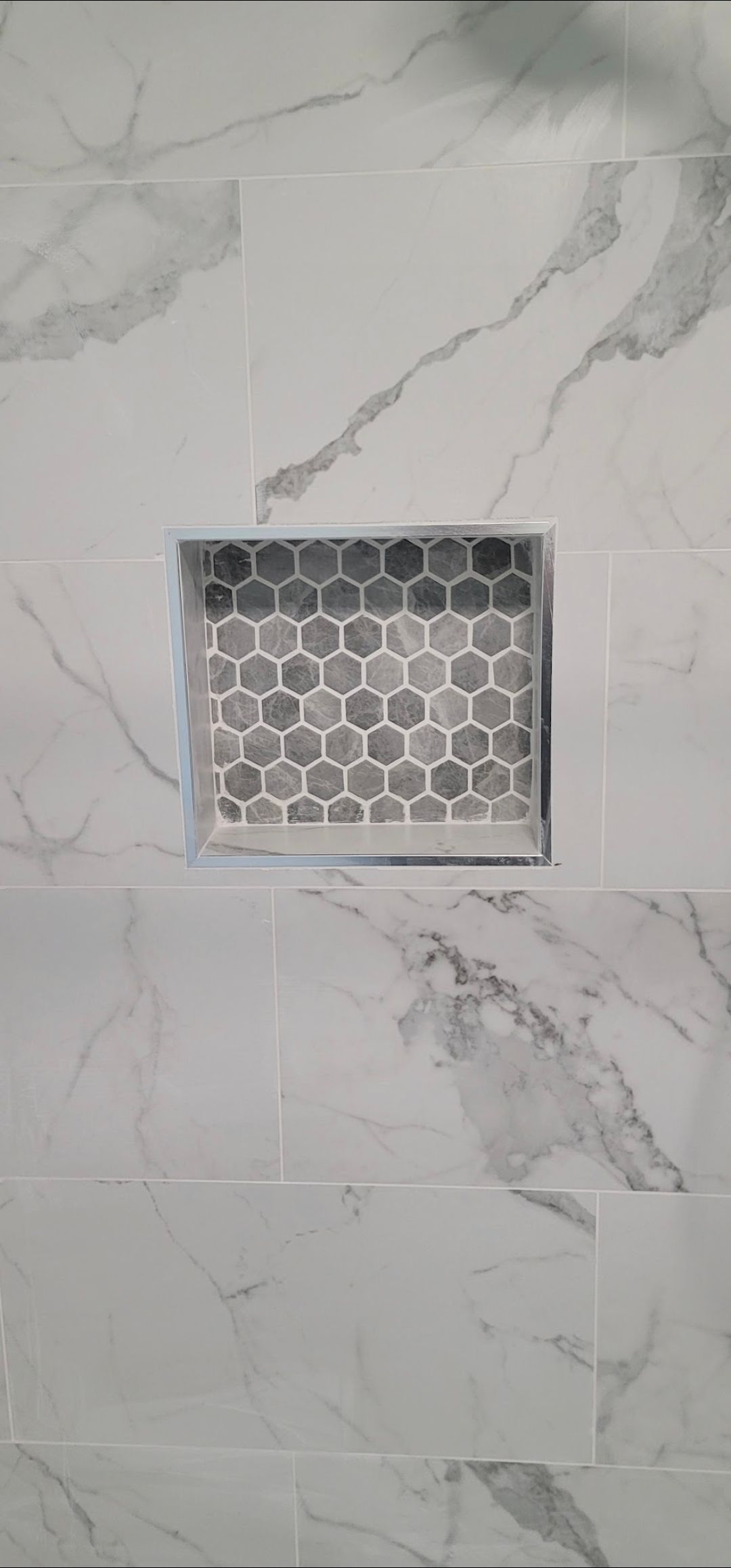 A shower niche in a bathroom with marble tiles and a honeycomb pattern.