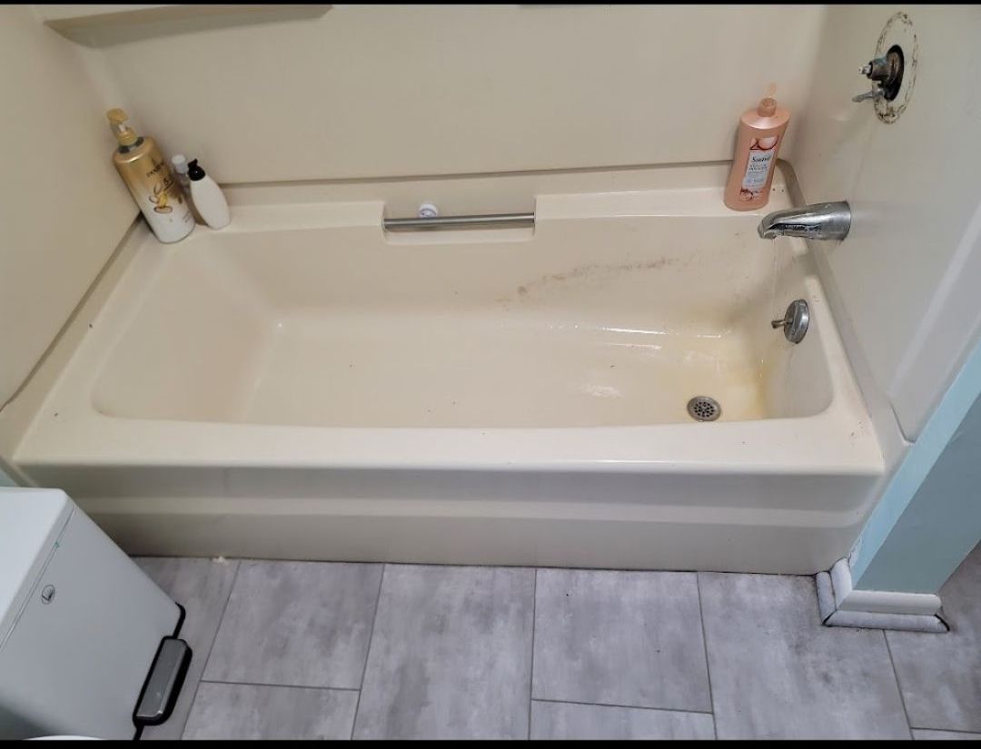 A bathtub in a bathroom next to a trash can.
