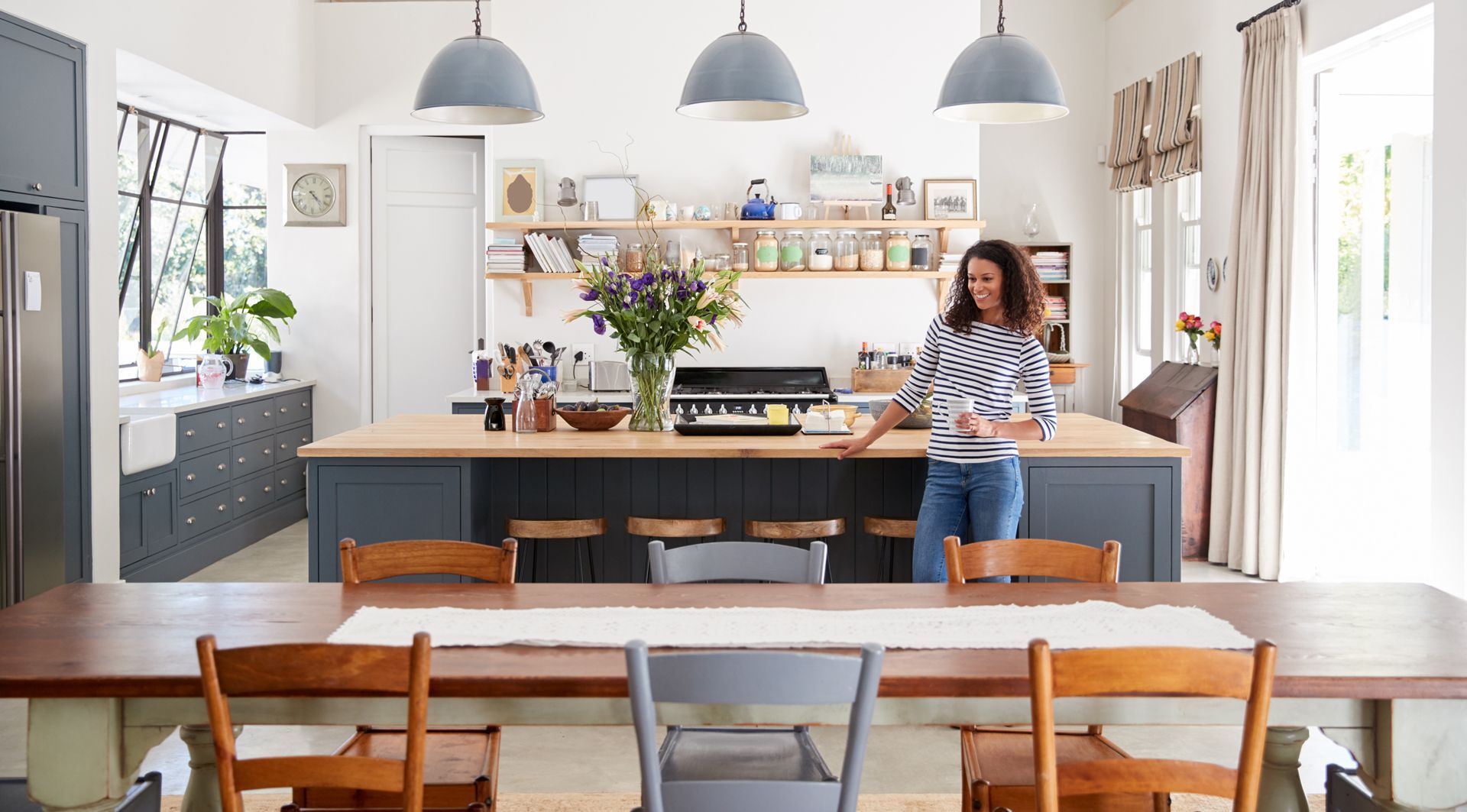 A woman is standing in a kitchen next to a dining table.