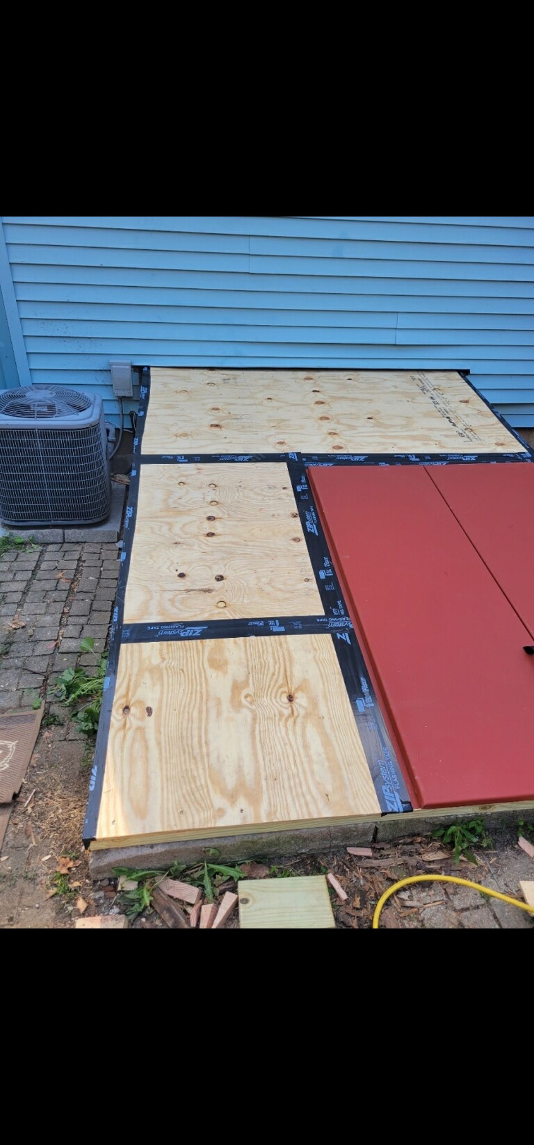 Outdoor wooden planks laid out in front of a blue building with a red painted door.