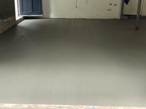 Gray concrete floor in a room, near a closed blue door and a white wall.