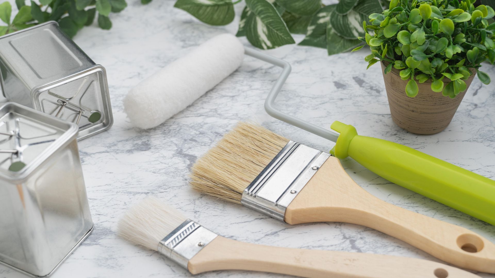 A group of paint brushes sitting on top of a table next to a plant.