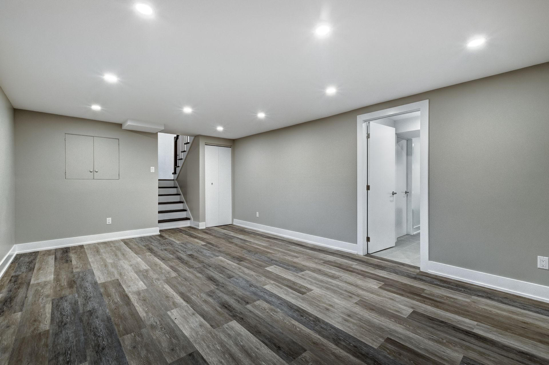 An empty basement with hardwood floors and stairs.