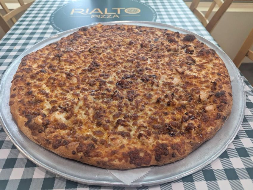 Large pizza on a silver tray. The pizza has a thick, browned crust and is topped with visible toppings.