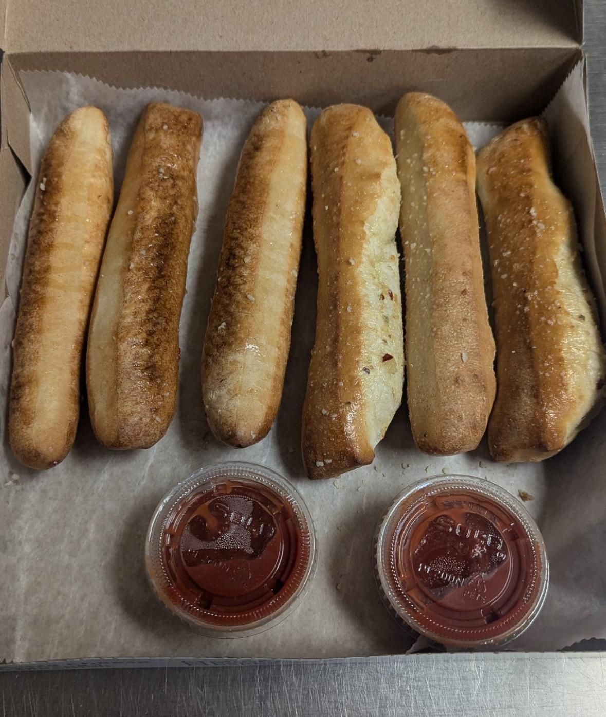 Breadsticks in a box with two small containers of red dipping sauce.