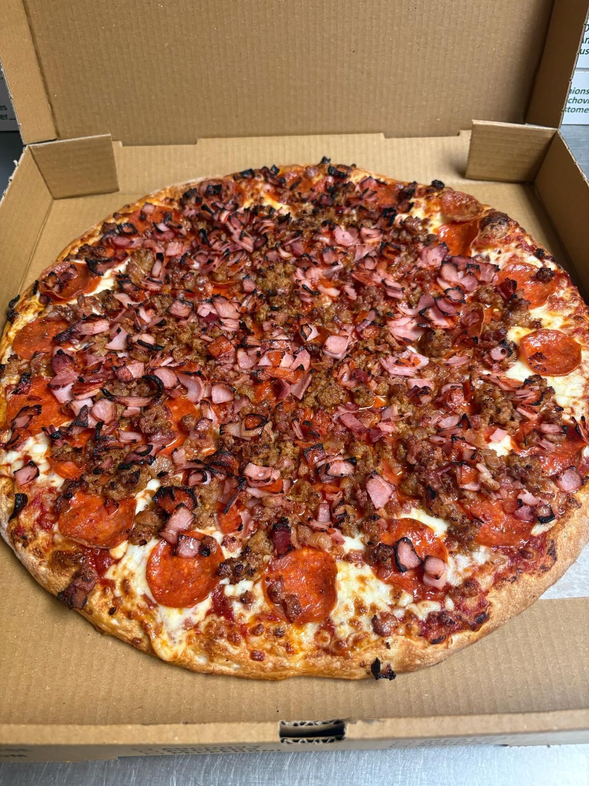 Pizza in a cardboard box, with pepperoni, meat, and a red sauce.