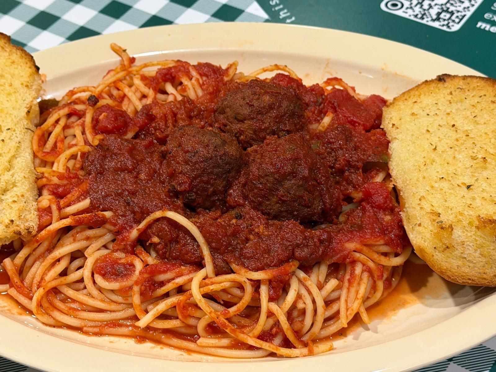 Spaghetti with meatballs and garlic bread on a plate, green checkered tablecloth.