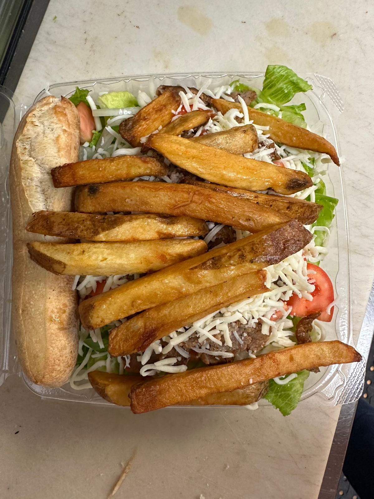 Salad with fries and bread in a clear container.