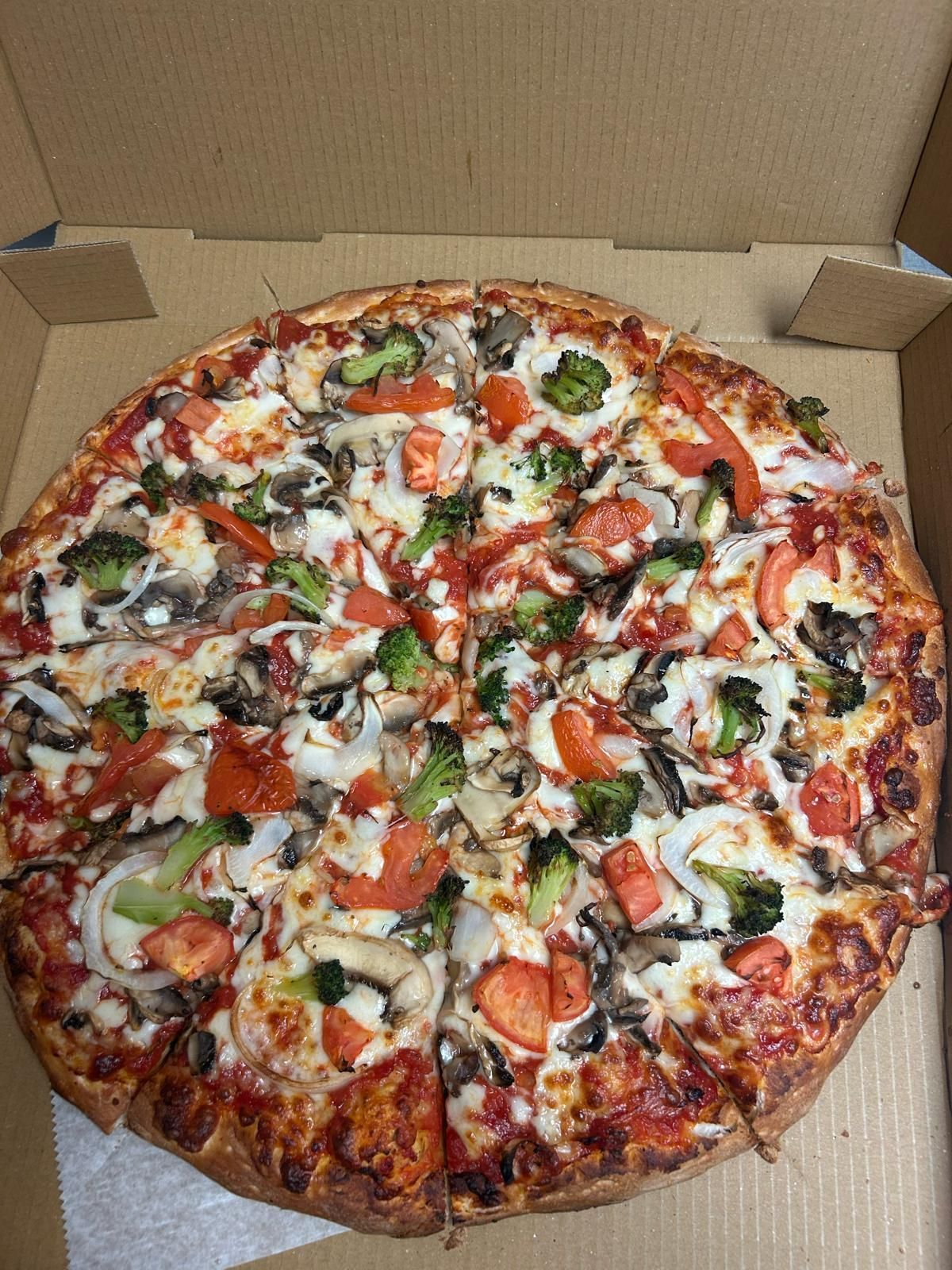 Pizza with broccoli, tomatoes, mushrooms, and onions in a cardboard box.