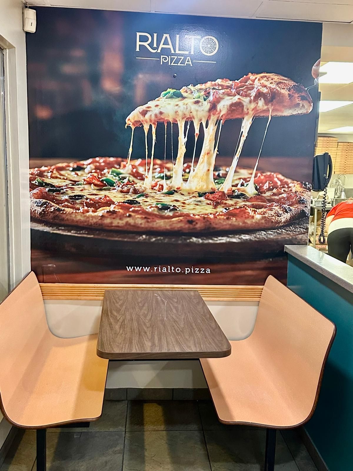 Booth seating in front of a Rialto Pizza mural showing a pizza with stretching cheese.