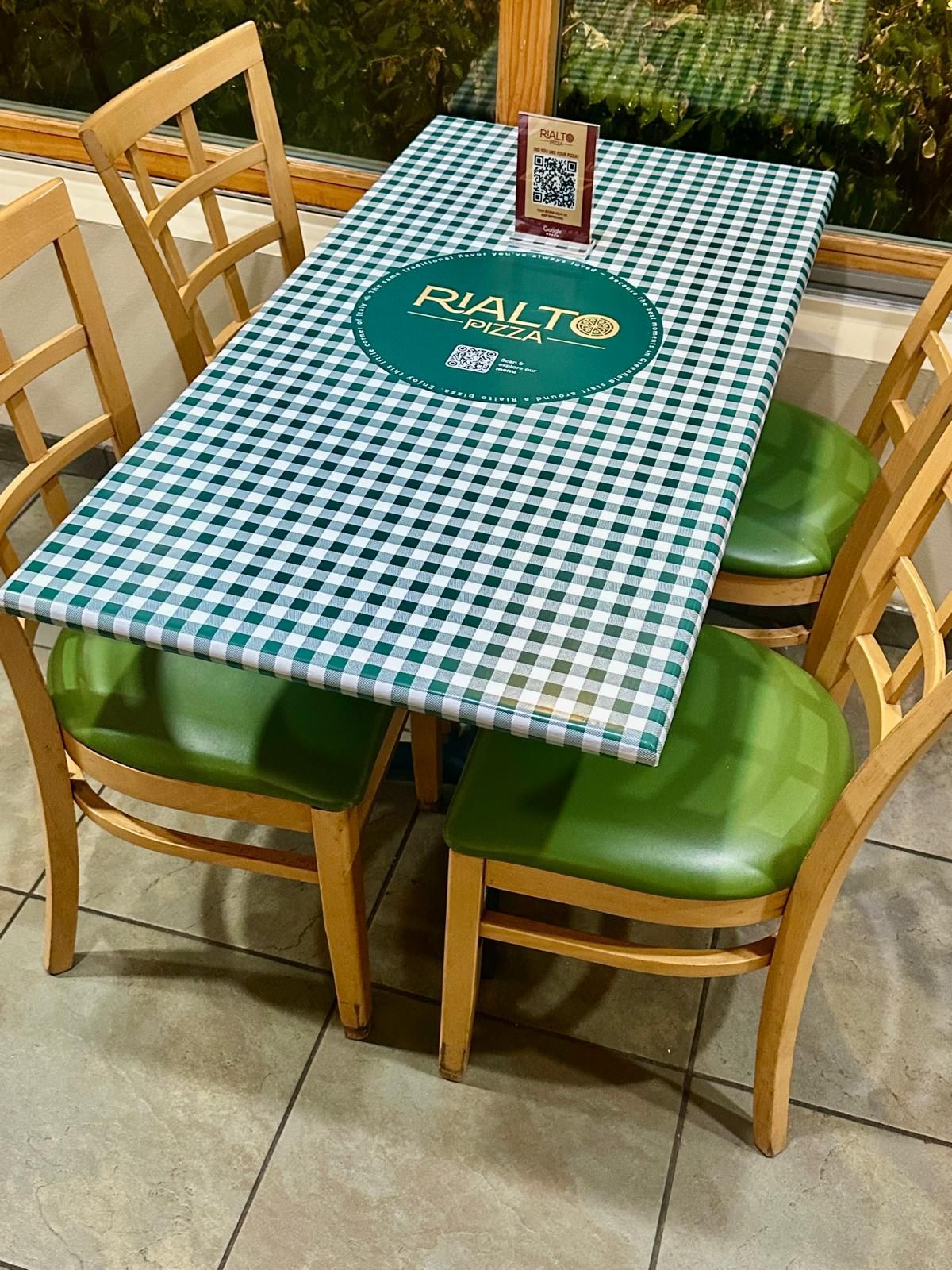 A dining table with a green and white checkered tablecloth and four green-padded chairs.